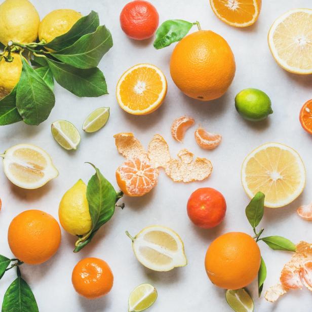 Verschiedene Zitrusfrüchte wie Zitronen, Orangen, Limetten und Mandarinen liegen auf einer hellen Oberfläche.