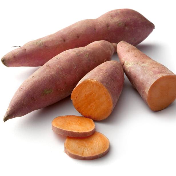 Mehrere Süßkartoffeln, einige davon angeschnitten, liegen auf einem weißen Hintergrund.