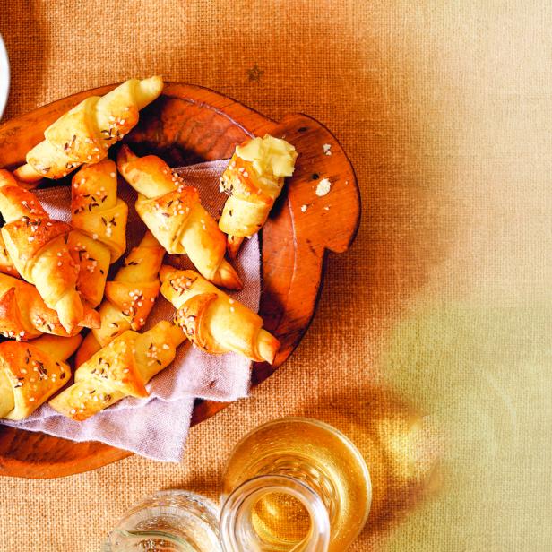 Salzige Croissants mit Kümmel in einer Holzschale, dazu Butter.