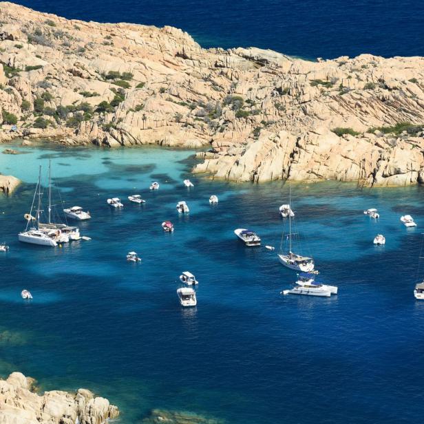 Zahlreiche Boote ankern in einer Bucht mit türkisfarbenem Wasser und Felsenküste.