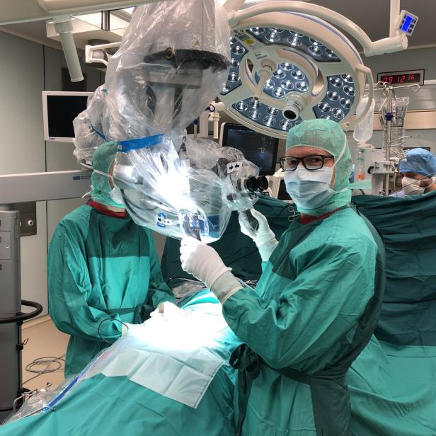Ein Operationsteam führt eine Operation mit einem Mikroskop in einem Operationssaal durch.