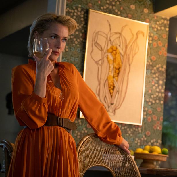 Gillian Anderson in einem orangefarbenen Kleid mit einem Glas Wein in der Hand.