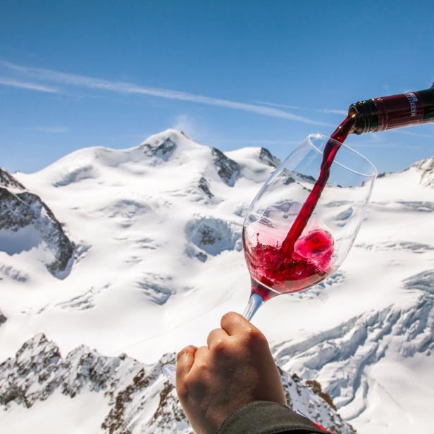 Vor einer verschneiten Berglandschaft wird Rotwein in ein Glas gegossen.
