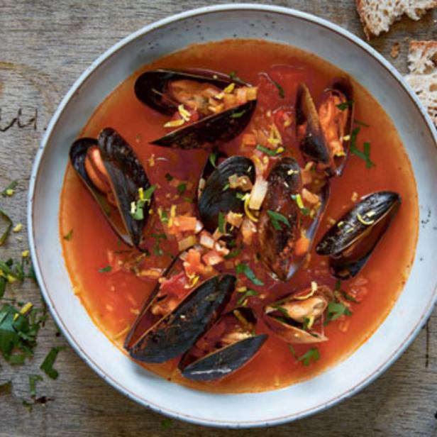 Eine Schüssel mit Miesmuscheln in Tomatensauce, serviert mit Brot.