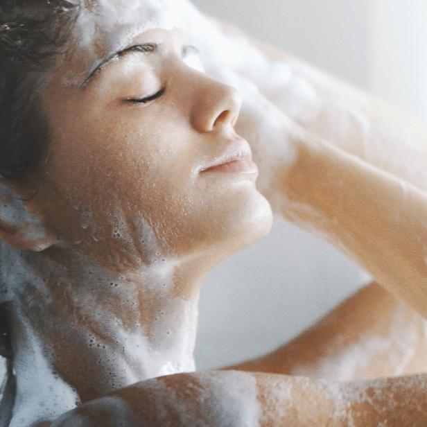 Eine Frau wäscht sich mit geschlossenen Augen die Haare unter der Dusche.
