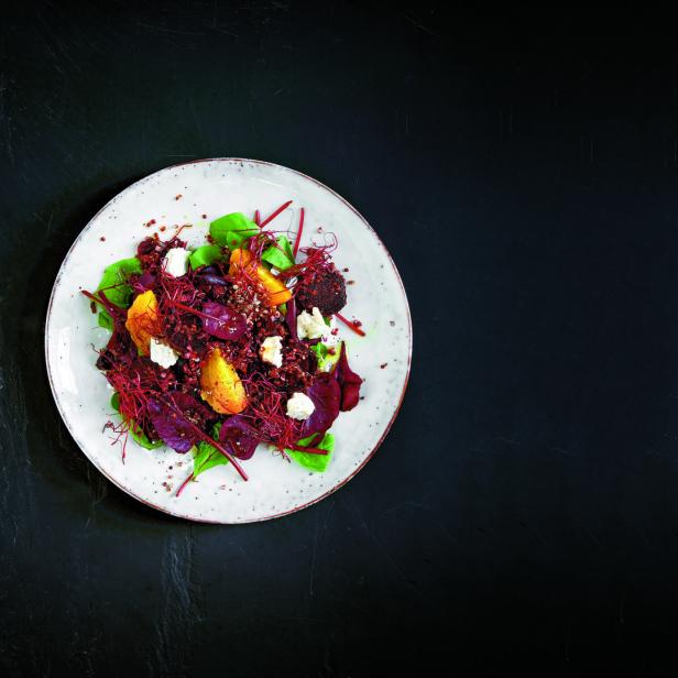 Ein Teller mit Rote-Bete-Salat, Orangenstücken und Ziegenkäse auf einem dunklen Hintergrund.