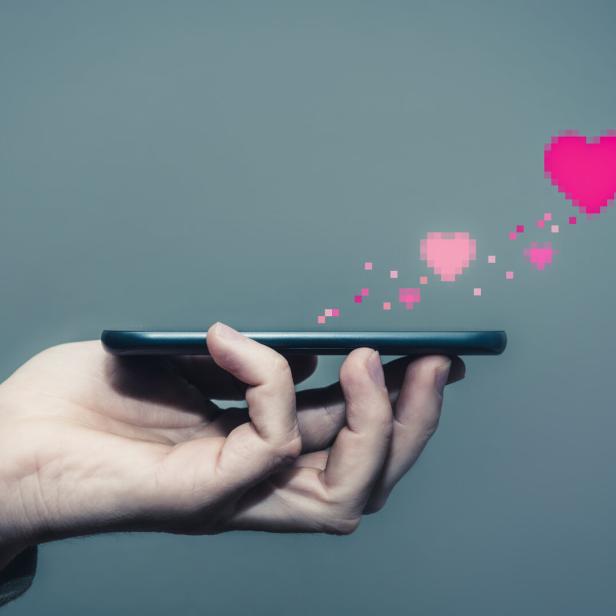 Eine Hand hält ein Smartphone, von dem Pixel-Herzen aufsteigen.