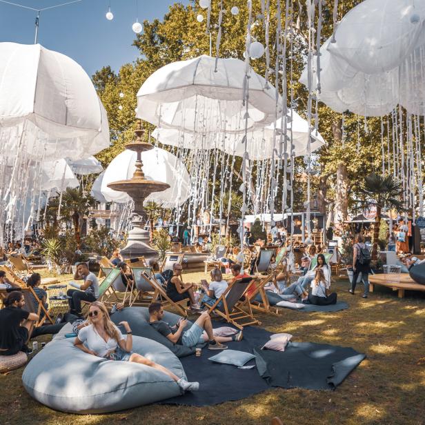 Menschen entspannen sich unter weißen, quallenartigen Dekorationen in einem Park.