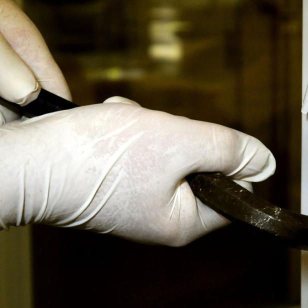 Eine Person mit Handschuhen bricht mit einem Brecheisen eine Tür auf.