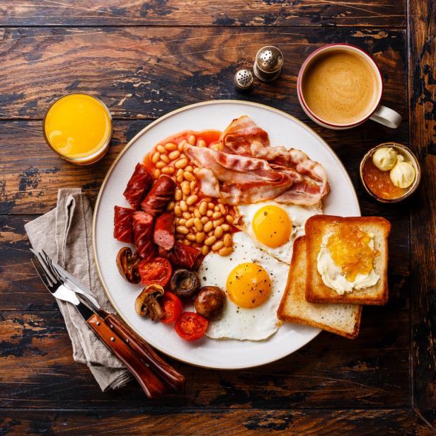 Ein komplettes englisches Frühstück mit Eiern, Speck, Bohnen und Toast auf einem Holztisch.