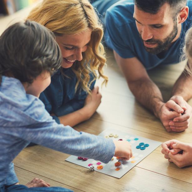 Eine Familie spielt gemeinsam ein Brettspiel auf dem Boden.