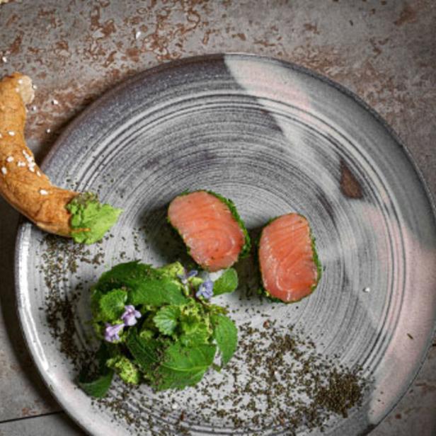Ein Teller mit zwei Scheiben Lachs, Kräutern und einem Brezelstück.