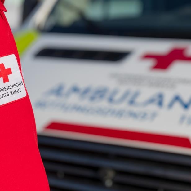 Eine Person in Rettungsjacke steht mit dem Rücken zur Kamera, im Hintergrund ist ein Rettungswagen zu sehen.