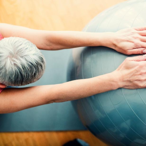 Eine Frau dehnt sich mit einem Gymnastikball auf einer Matte.