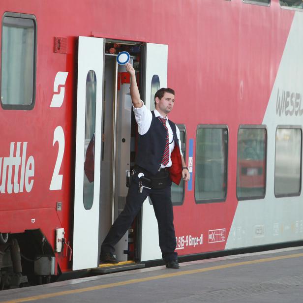 Ein Zugbegleiter steht in der Tür eines CityShuttle-Zuges und hält eine blaue Kelle hoch.