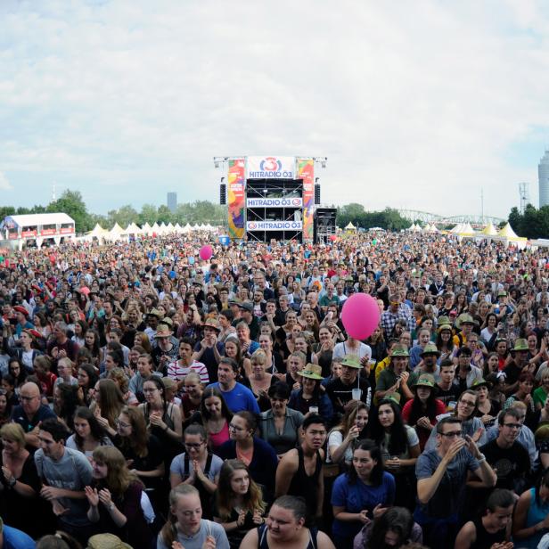 Eine große Menschenmenge jubelt vor einer Bühne von Hitradio Ö3 mit dem Donauturm im Hintergrund.