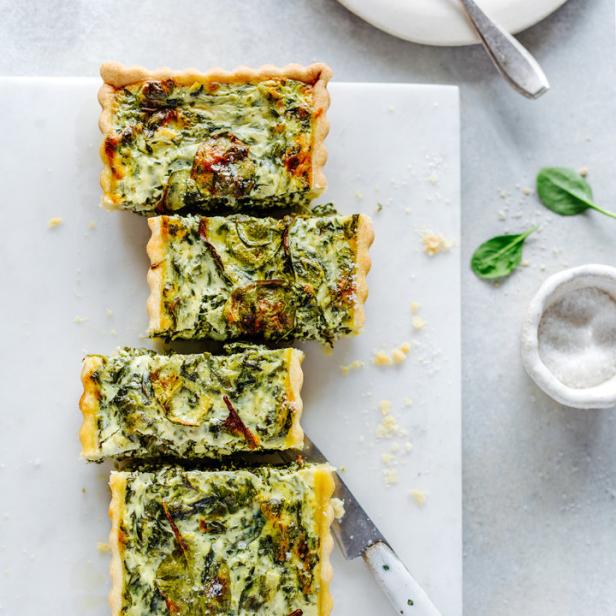 Eine angeschnittene Spinatquiche liegt auf einem weißen Marmorbrett.