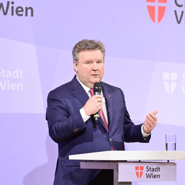 Ein Mann in einem Anzug spricht bei einer Veranstaltung der Stadt Wien in ein Mikrofon.