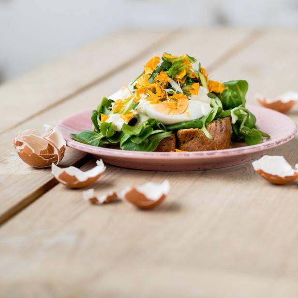 Ein belegtes Brot mit Ei, Salat und essbaren Blüten auf einem rosa Teller.