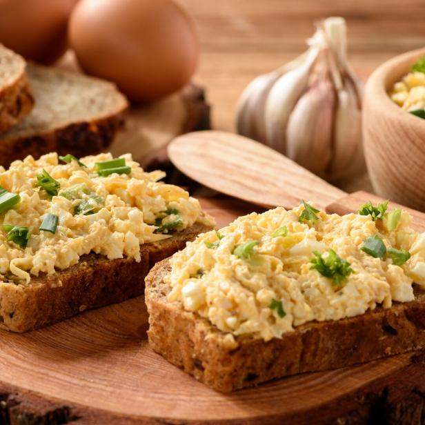 Zwei Brotscheiben belegt mit Eiersalat und Schnittlauch auf einem Holzbrett.