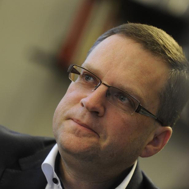Ein Mann mit Brille und Anzug blickt nachdenklich nach oben.