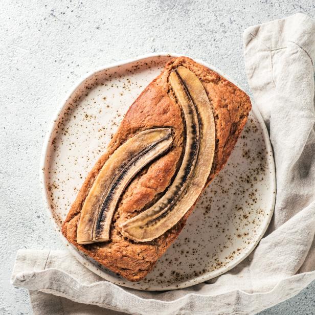 Ein Bananenbrot liegt auf einem Teller neben einem Leinentuch.