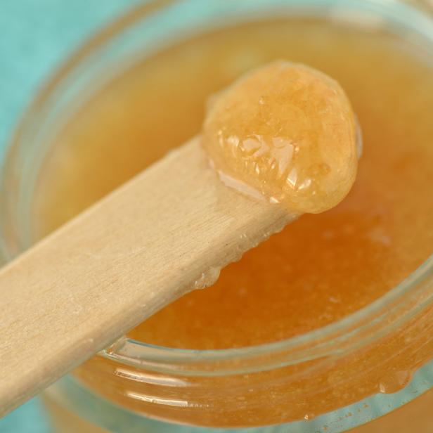 Ein Glas mit einem orangefarbenen Zuckerpeeling und einem Holzspatel.