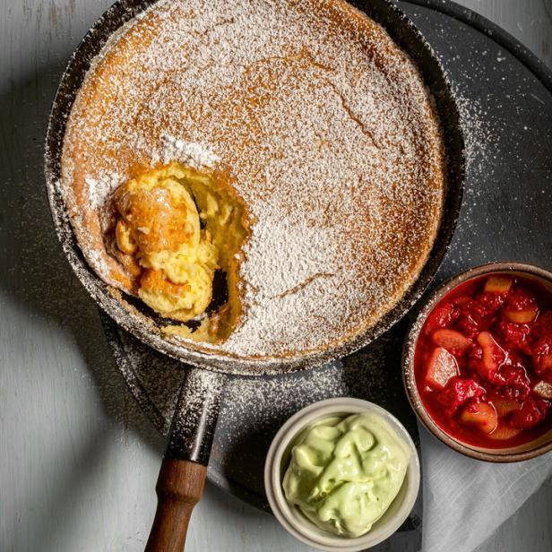 Ein Dutch Baby Pfannkuchen mit Puderzucker, Eis und Erdbeersalat in einer Bratpfanne.