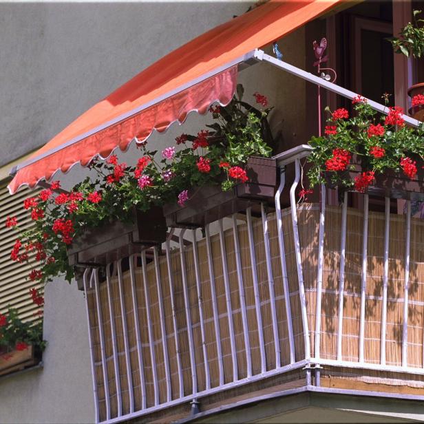 Ein Balkon mit roter Markise und üppigen Geranienkästen.