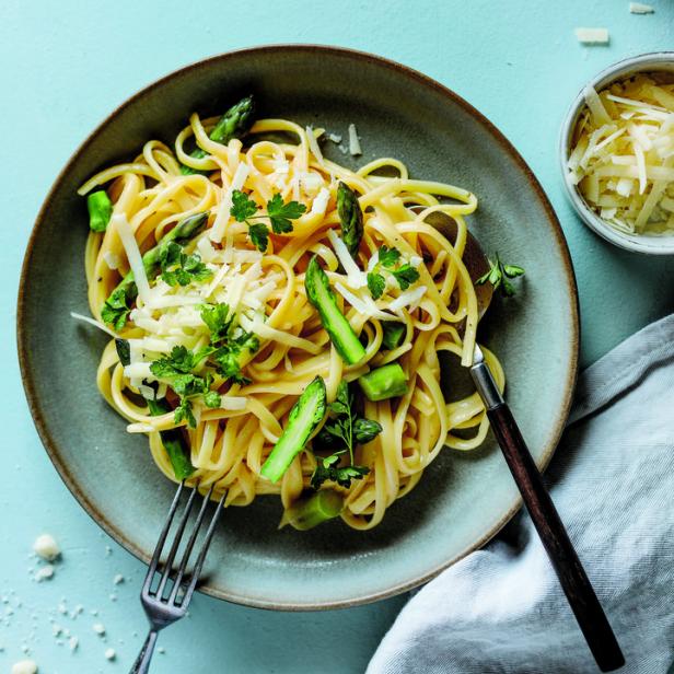 Ein Teller Linguine mit Spargel, Parmesan und Petersilie auf blauem Hintergrund.