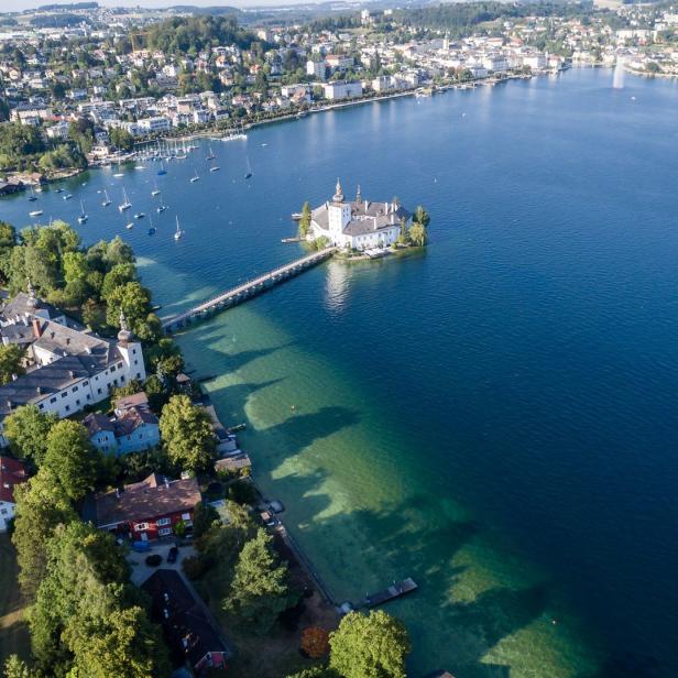 Luftaufnahme von Schloss Ort auf einer Insel im Traunsee mit einer Brücke zum Ufer.