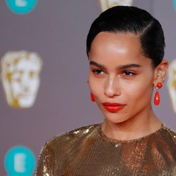 Zoë Kravitz auf dem roten Teppich mit goldenem Kleid und roten Ohrringen.