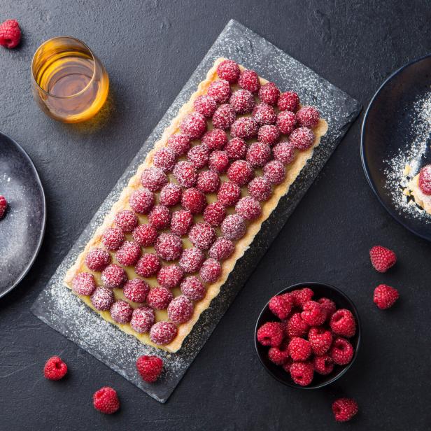 Rechteckige Himbeertarte und Tartelettes auf Tellern, mit Puderzucker bestäubt.