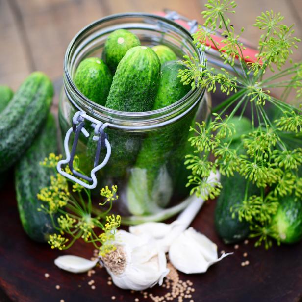 Einmachglas mit Gurken, Dill und Knoblauch auf einem Holzbrett.