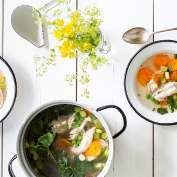 Eine Hühnersuppe mit Karotten, Erbsen und Kräutern wird serviert.