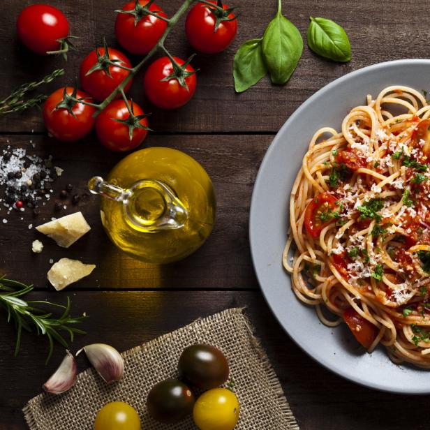 Ein Teller Spaghetti mit Tomatensauce, Basilikum und geriebenem Käse auf einem Holztisch.