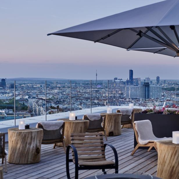 Eine Dachterrasse mit Blick auf Wien bei Dämmerung.