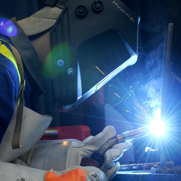 Ein Schweißer arbeitet mit Schutzkleidung und Helm an einem Werkstück.