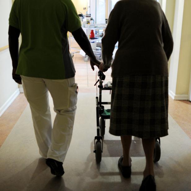 Pflegekraft hilft alter Frau mit Rollator im Pflegeheim.
