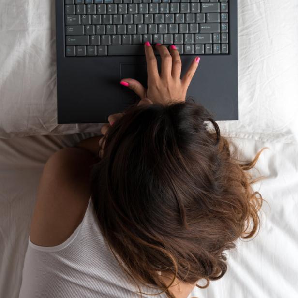 Eine Frau liegt im Bett und tippt auf einem Laptop.
