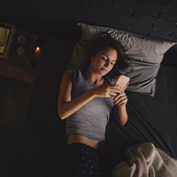 Eine Frau liegt im Bett und schaut auf ihr Handy.