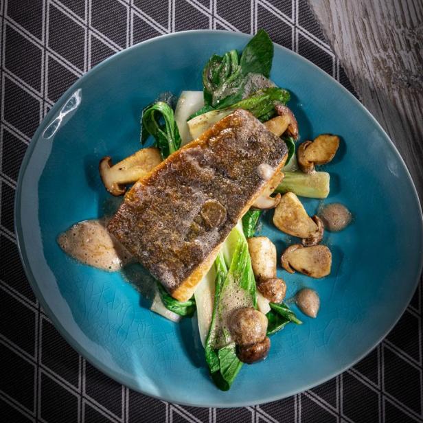 Ein Teller mit gebratenem Fisch, Gemüse und Pilzen auf einem Tisch.
