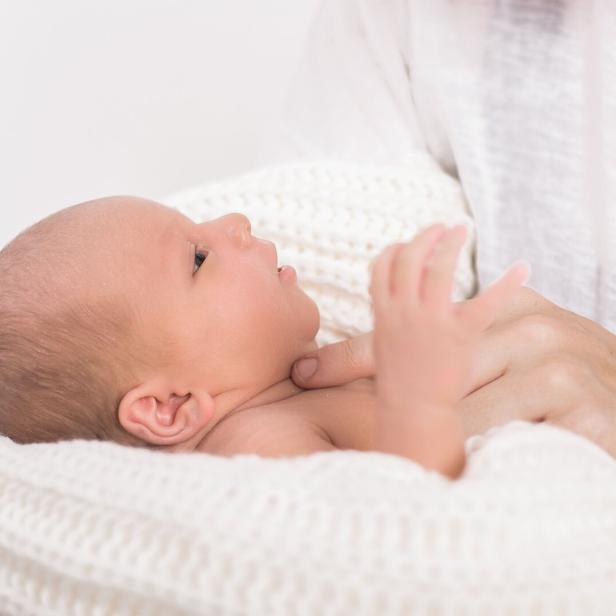 Ein Neugeborenes liegt in einer weißen Decke und wird von einer Person im Arm gehalten.