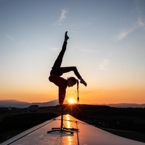 Eine Frau macht bei Sonnenuntergang eine Handstand-Akrobatik auf einem Dach.