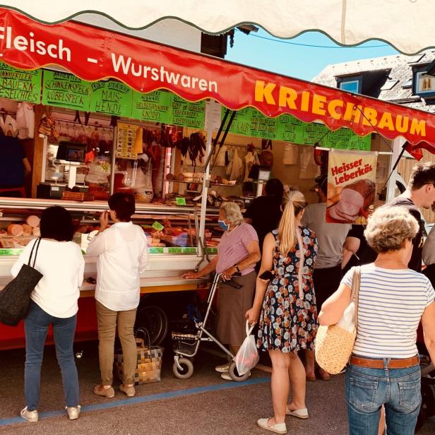 Kunden stehen an einem Stand mit Fleisch- und Wurstwaren auf einem Markt.