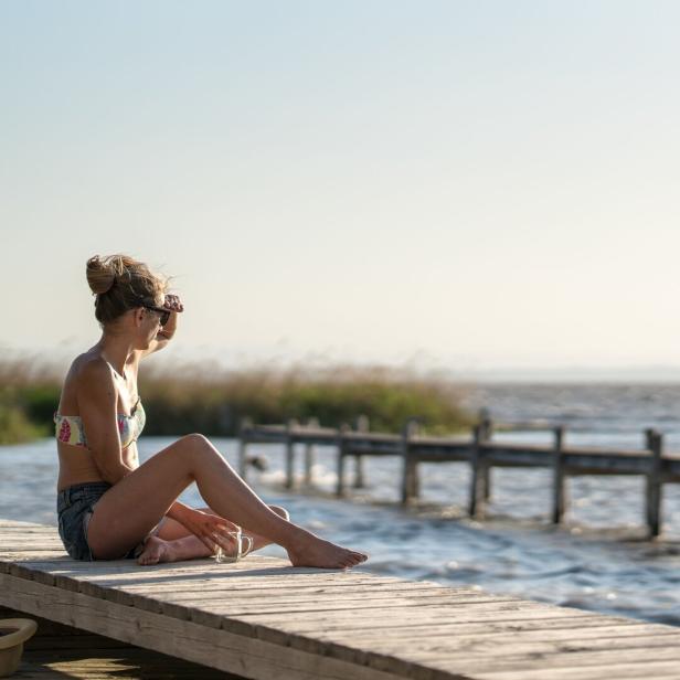 Eine Frau sitzt auf einem Steg in Podersdorf und schaut aufs Wasser.