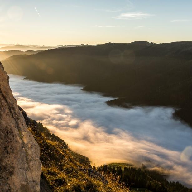 Die Sonne scheint über eine nebelverhangene Berglandschaft.