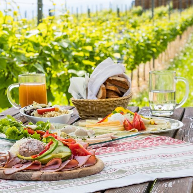 Ein Picknicktisch mit Speisen und Getränken vor einem Weinberg.