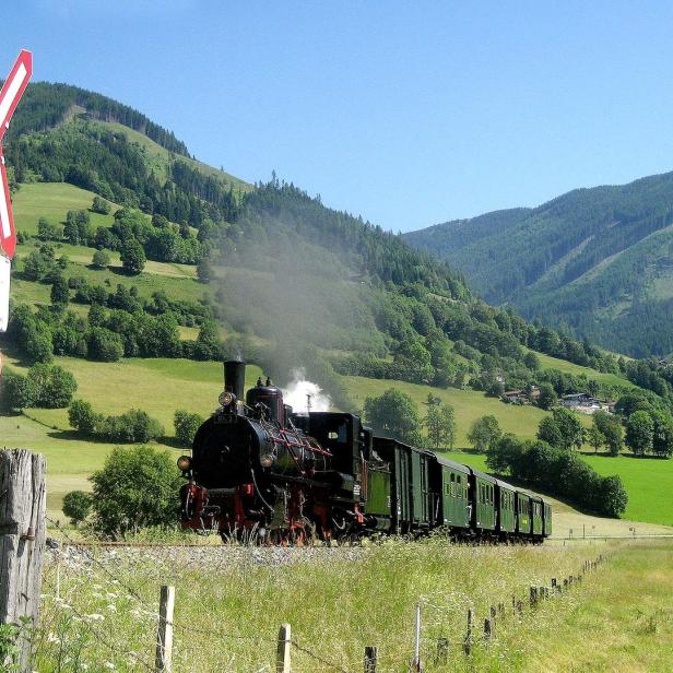 Eine Dampflokomotive fährt durch eine grüne Landschaft mit Bergen im Hintergrund.