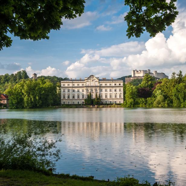 Schloss Leopoldskron am Ufer eines Sees mit der Festung Hohensalzburg im Hintergrund.